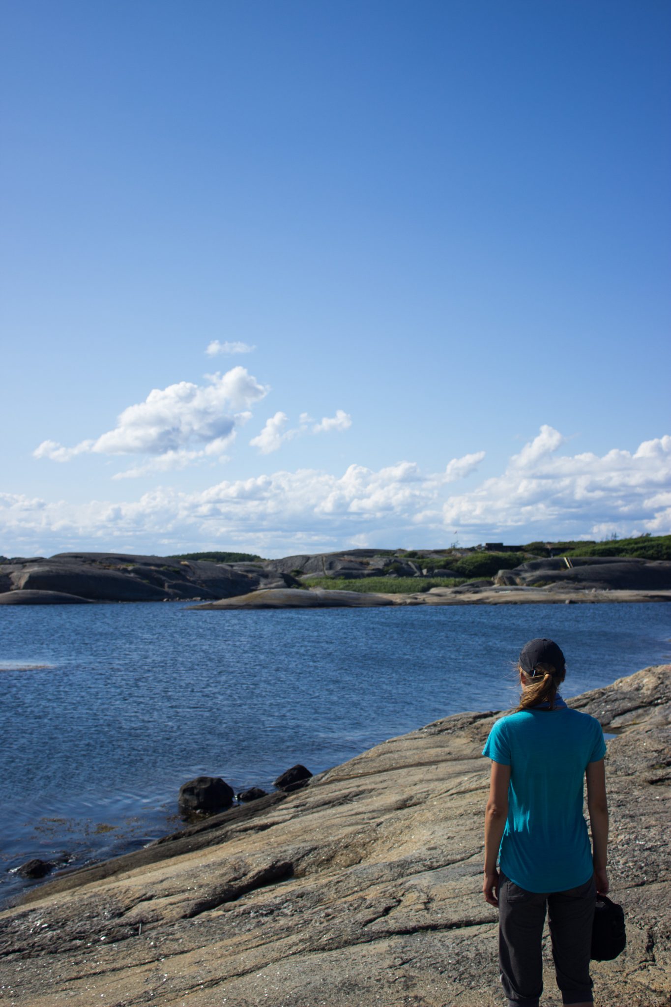 Küstenwanderung von Stavern nach Nevlunghavn, auf dem Kyststien entlang der Schärenküste von Vestfold in Südnorwegen, Wanderung entlang des Küstenpfads, Wegverlauf über große Felsen mit Meerblick und grüner Vegetation, Wanderer genießt schönes Wetter und die Aussicht