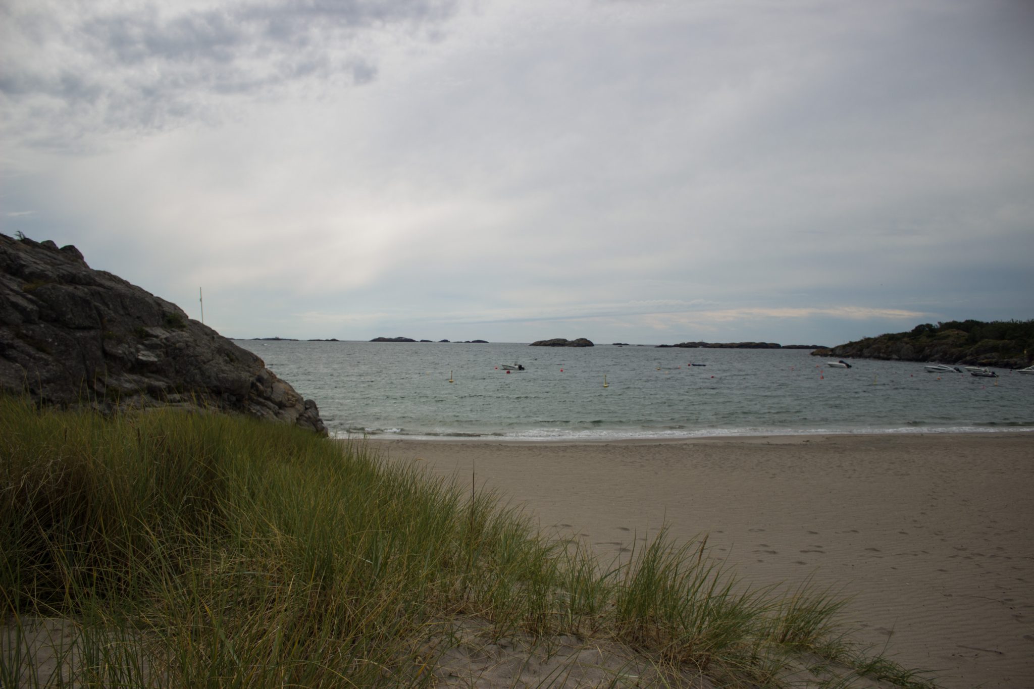 Küstenwanderung von Stavern nach Nevlunghavn, auf dem Kyststien entlang der Schärenküste von Vestfold in Südnorwegen, Wanderung entlang des Küstenpfads, kleiner Sandstrand mit Schilf und Felsen entlang des Wanderweges, Meer und Felsen im Hintergrund