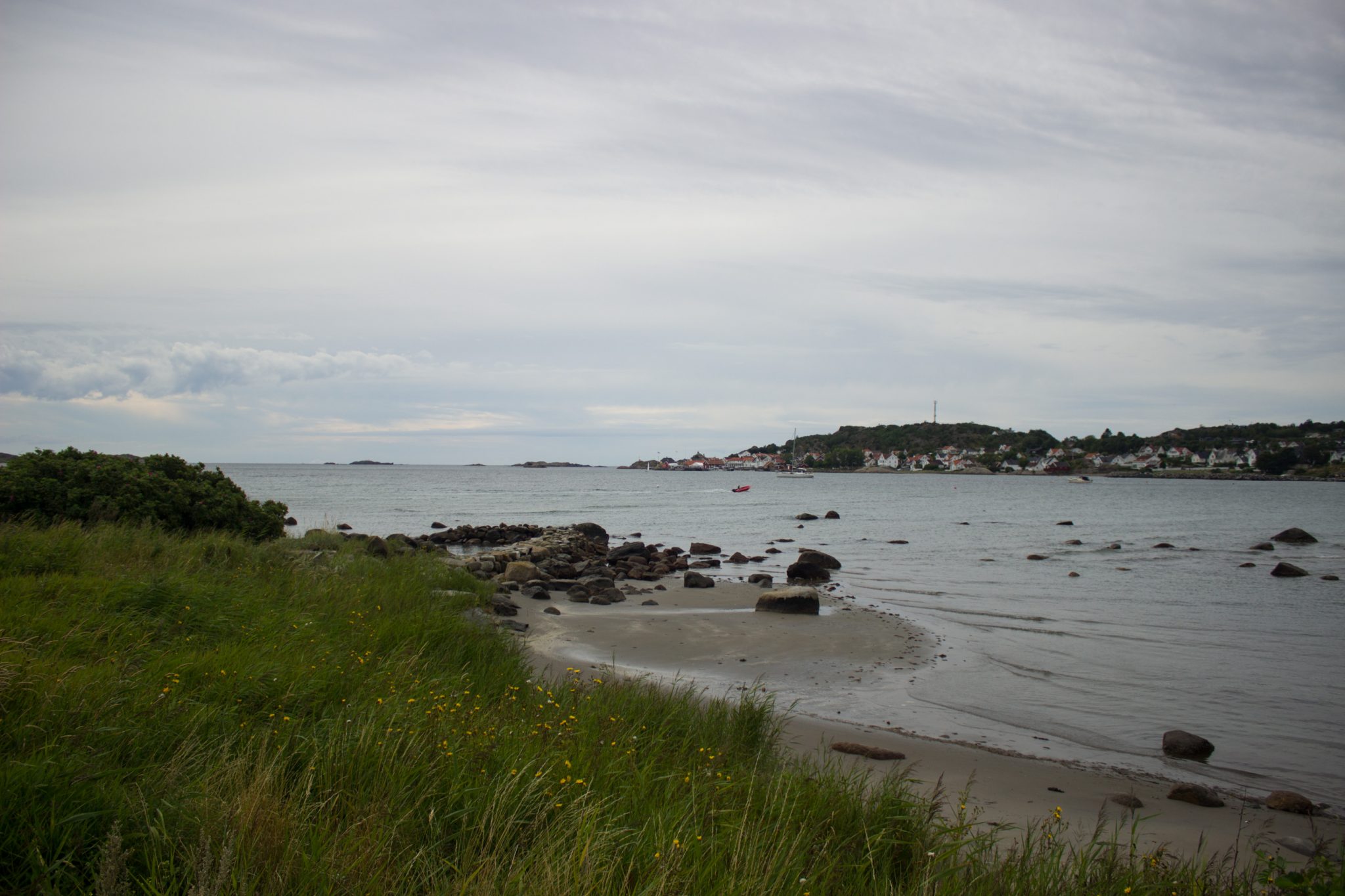 Küstenwanderung von Stavern nach Nevlunghavn, auf dem Kyststien entlang der Schärenküste von Vestfold in Südnorwegen, Wanderung entlang des Küstenpfads, kleiner Sandstrand mit Schilf und Steinen entlang des Wanderweges, kleiner Ort auf der anderen Seite der Bucht, Aussicht auf das Meer