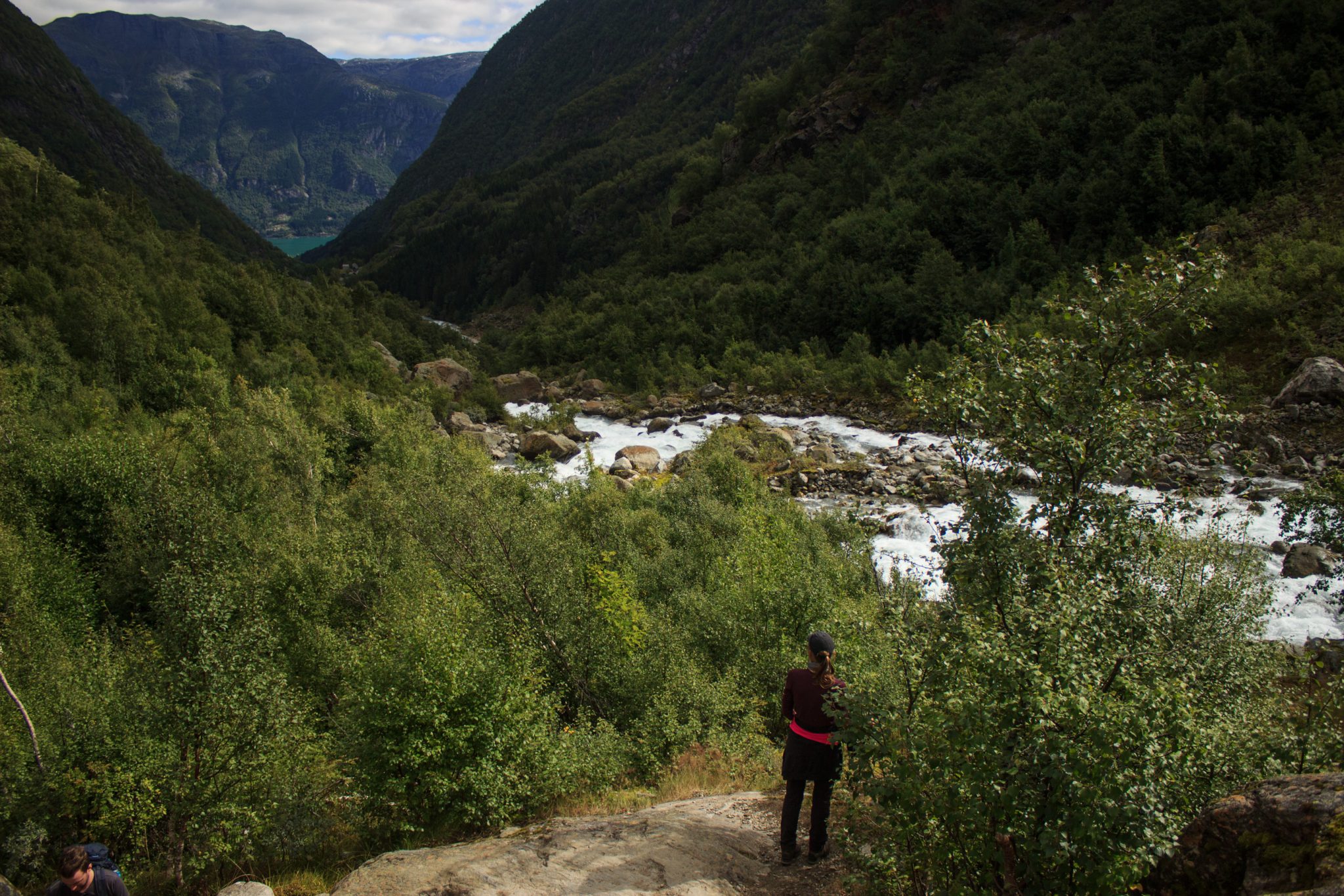 Wandern zum Buarbreen im Folgefonna Nationalpark, Wanderung in der Nähe von Odda mit Aussicht auf den Gletscher Buarbreen und Wasserfälle, Wanderer genießt Aussicht auf den strömenden Fluss und die Berge auf der gegenüberliegenden Seite vom Gletscher Bondusbreen