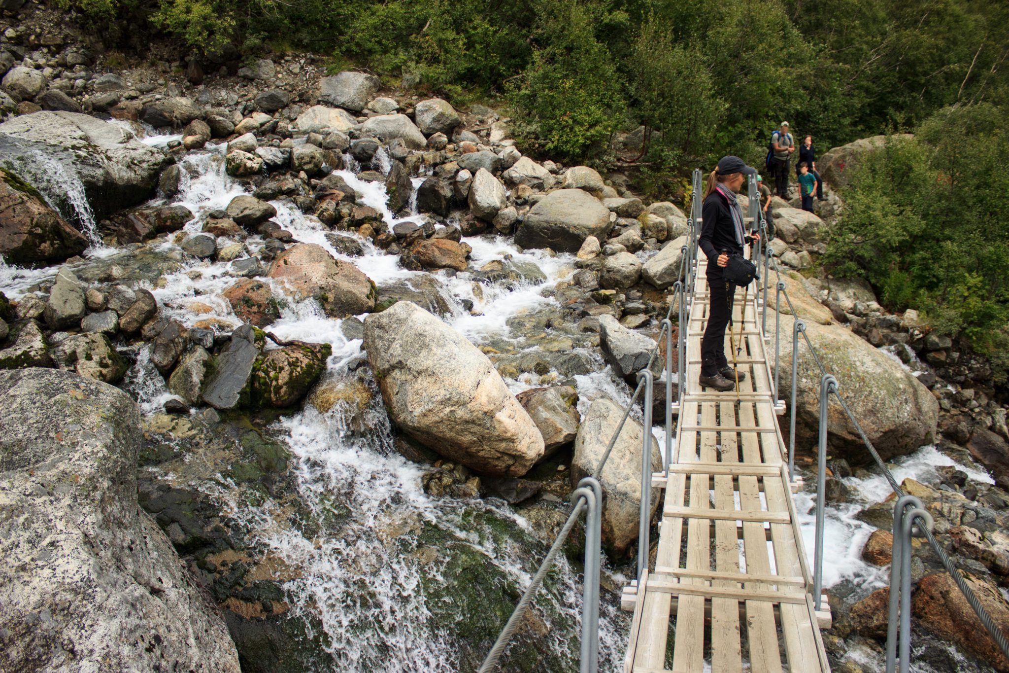 Wandern zum Buarbreen im Folgefonna Nationalpark, Wanderung in der Nähe von Odda mit Aussicht auf den Gletscher Buarbreen und Wasserfälle, Wanderer steht auf Brücke, die während der Wanderung über den Fluss führt