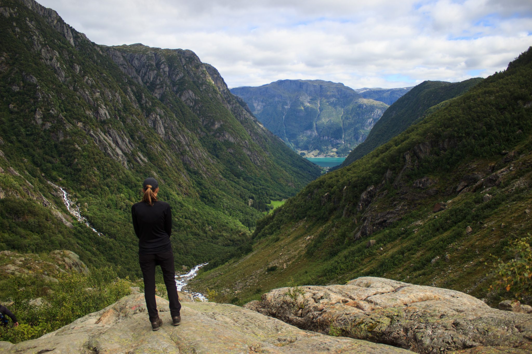 Wandern zum Buarbreen im Folgefonna Nationalpark, Wanderung in der Nähe von Odda mit Aussicht auf den Gletscher Buarbreen und Wasserfälle, Wanderer genießt Aussicht auf den strömenden Fluss im Tal und die Berge auf der gegenüberliegenden Seite vom Gletscher Bondusbreen