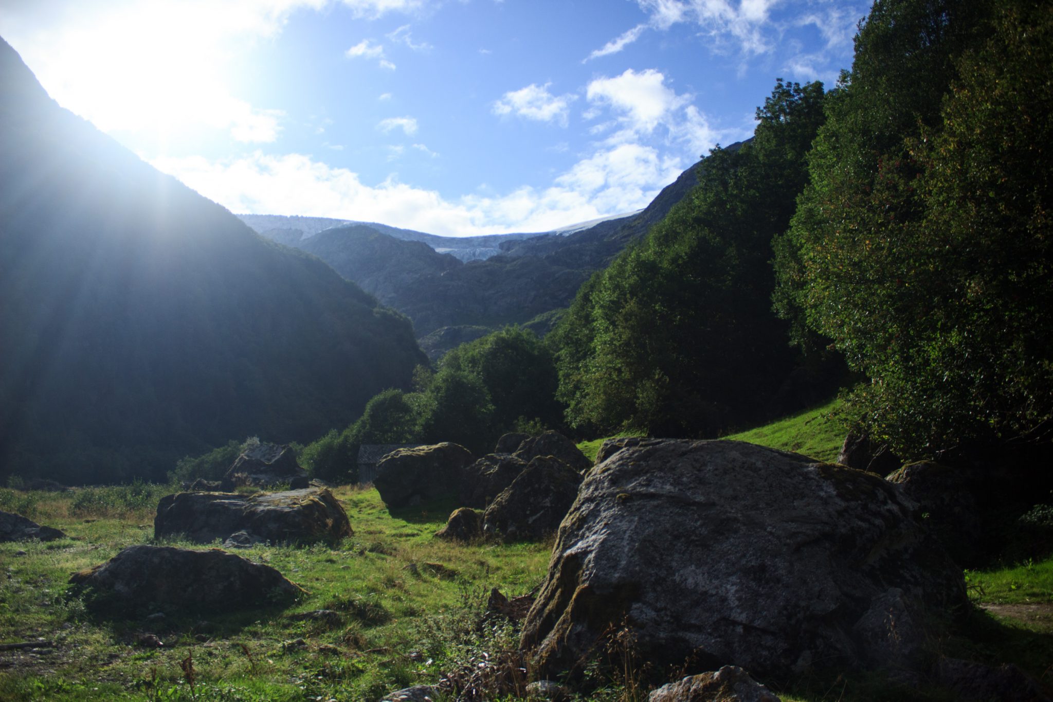 Wandern zum Buarbreen im Folgefonna Nationalpark, Wanderung in der Nähe von Odda mit Aussicht auf den Gletscher Buarbreen und Wasserfälle, Blick auf den Gletscher Buarbreen und den Wald unten im Tal, die Sonne sinkt langsam hinter die Berge