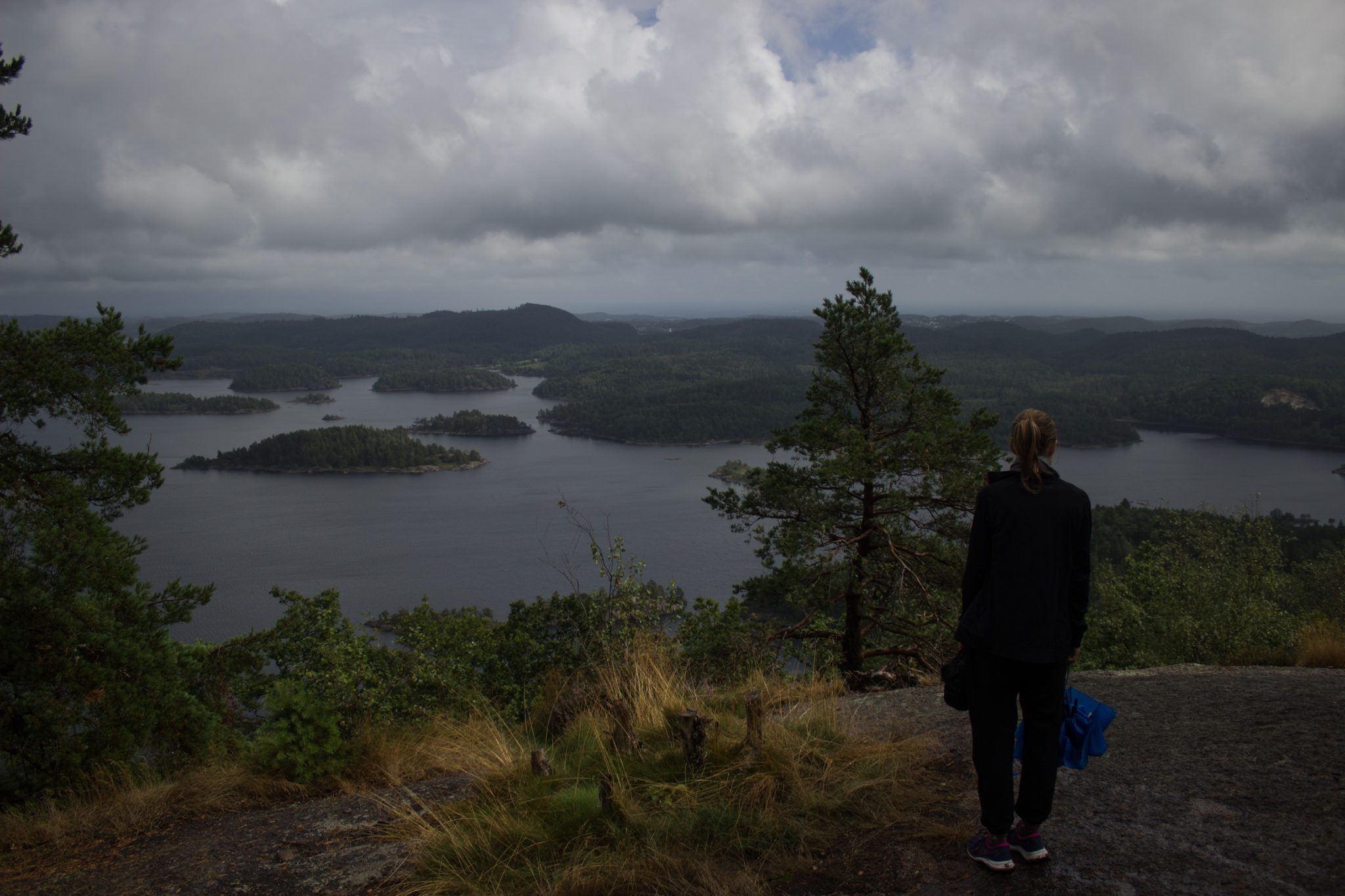 Wanderung im Rossefjellet Naturreservat - Teil der Rundwanderung bei Grimstad in Südnorwegen, nach Wanderung durch schönen und dichten Wald erblickt man diese traumhafte und weite Aussicht auf die umliegenden Seen und kleinen Inseln, dicht mit Wald bewachsene Umgebung, unterwegs in der Natur, Wanderer genießt Aussicht
