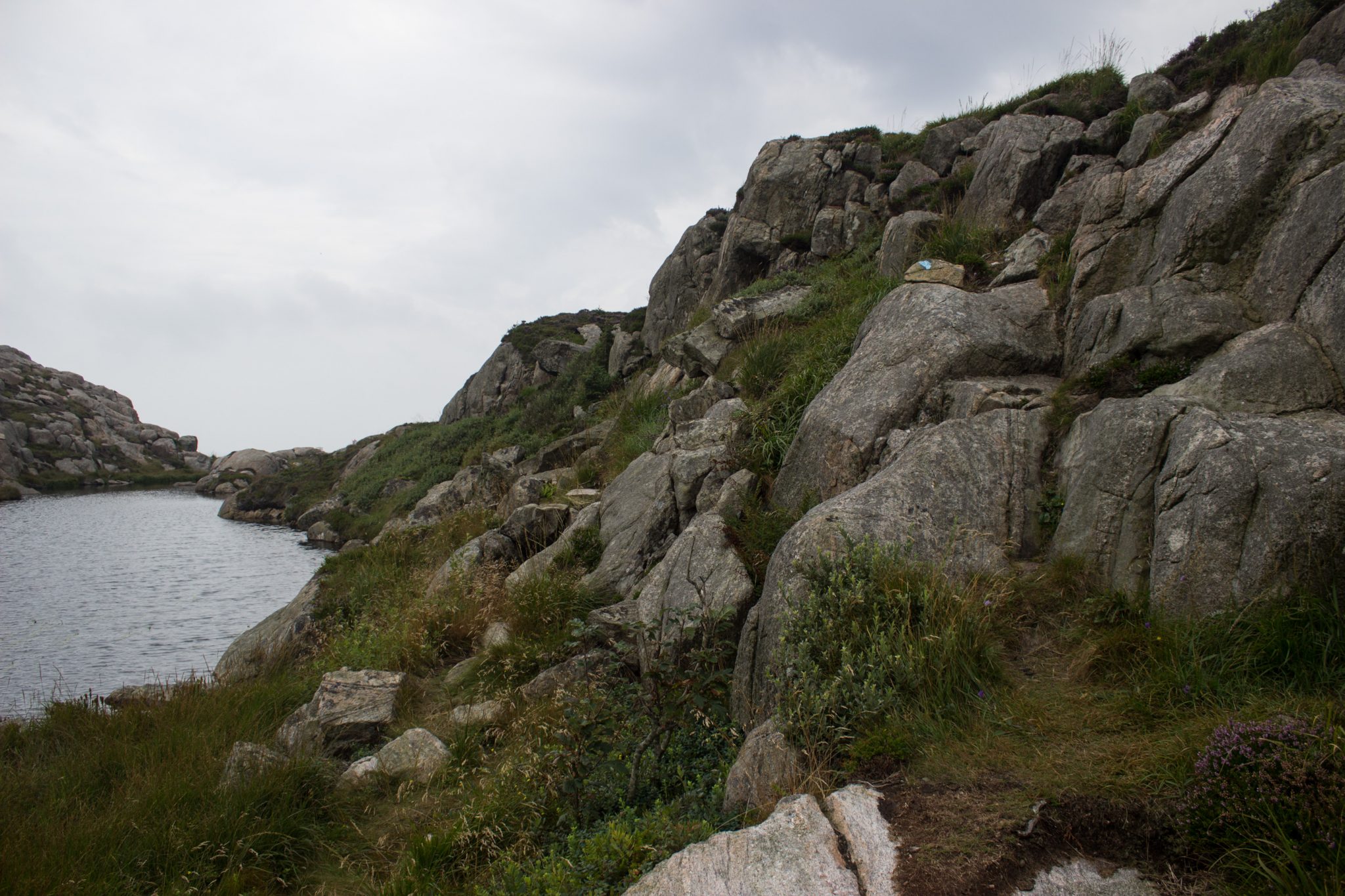 Wanderungen beim Kap Lindesnes, südlichster Punkt Norwegens, am Südkap in Norwegen, Wanderer unterwegs auf schmalem Pfad entlang großer Felsen, grüne Vegetation an der Küste, Heidelandschaft, Aussicht auf das weite Meer und einem kleinen See
