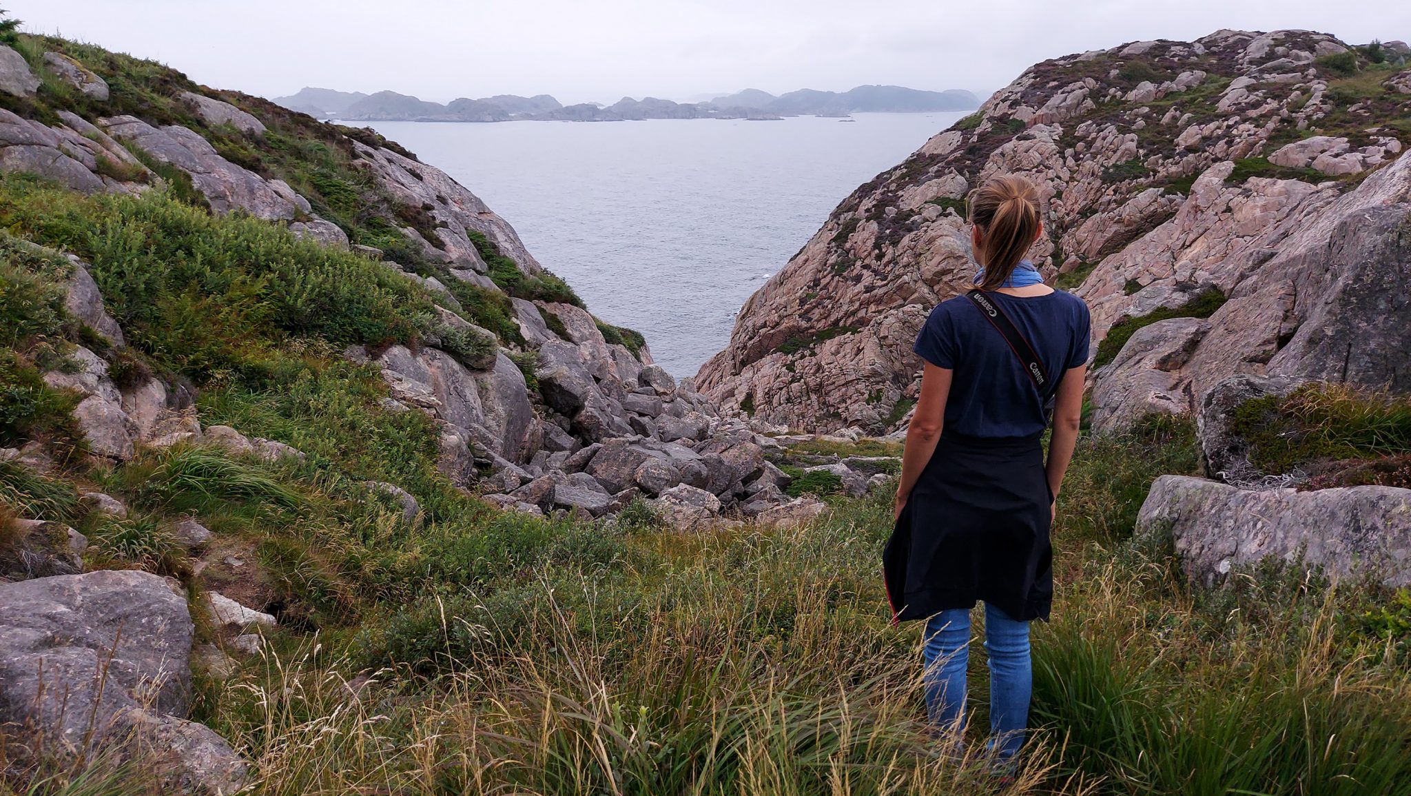 Wanderungen beim Kap Lindesnes, südlichster Punkt Norwegens, am Südkap in Norwegen, Wanderer unterwegs auf schmalem Pfad entlang großer Felsen, grüne Vegetation an der Küste, Heidelandschaft, Aussicht auf das weite Meer und kleine Inseln