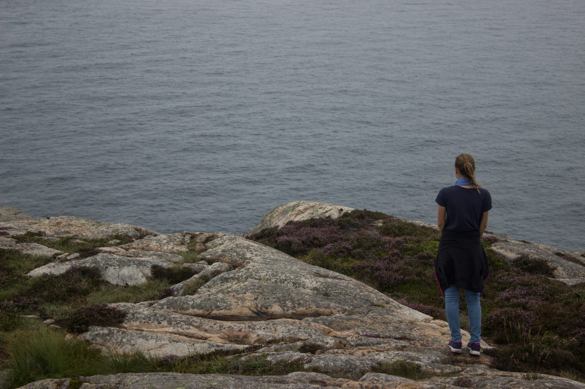 Wanderungen beim Kap Lindesnes, südlichster Punkt Norwegens, am Südkap in Norwegen, Wanderer genießt die Aussicht auf das weite Meer während der Wanderung beim Leuchtturm Lindesnes Fyr, unterwegs auf schmalem Pfad entlang großer Felsen, grüne Vegetation an der Küste, Heidelandschaft