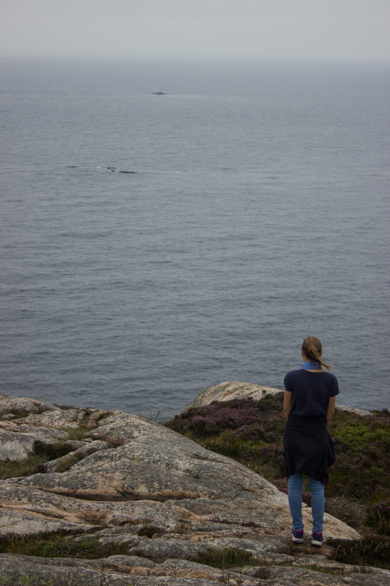 Wanderungen beim Kap Lindesnes, südlichster Punkt Norwegens, am Südkap in Norwegen, Wanderer genießt die Aussicht auf das weite Meer während der Wanderung beim Leuchtturm Lindesnes Fyr, unterwegs auf schmalem Pfad entlang großer Felsen, grüne Vegetation an der Küste, Heidelandschaft