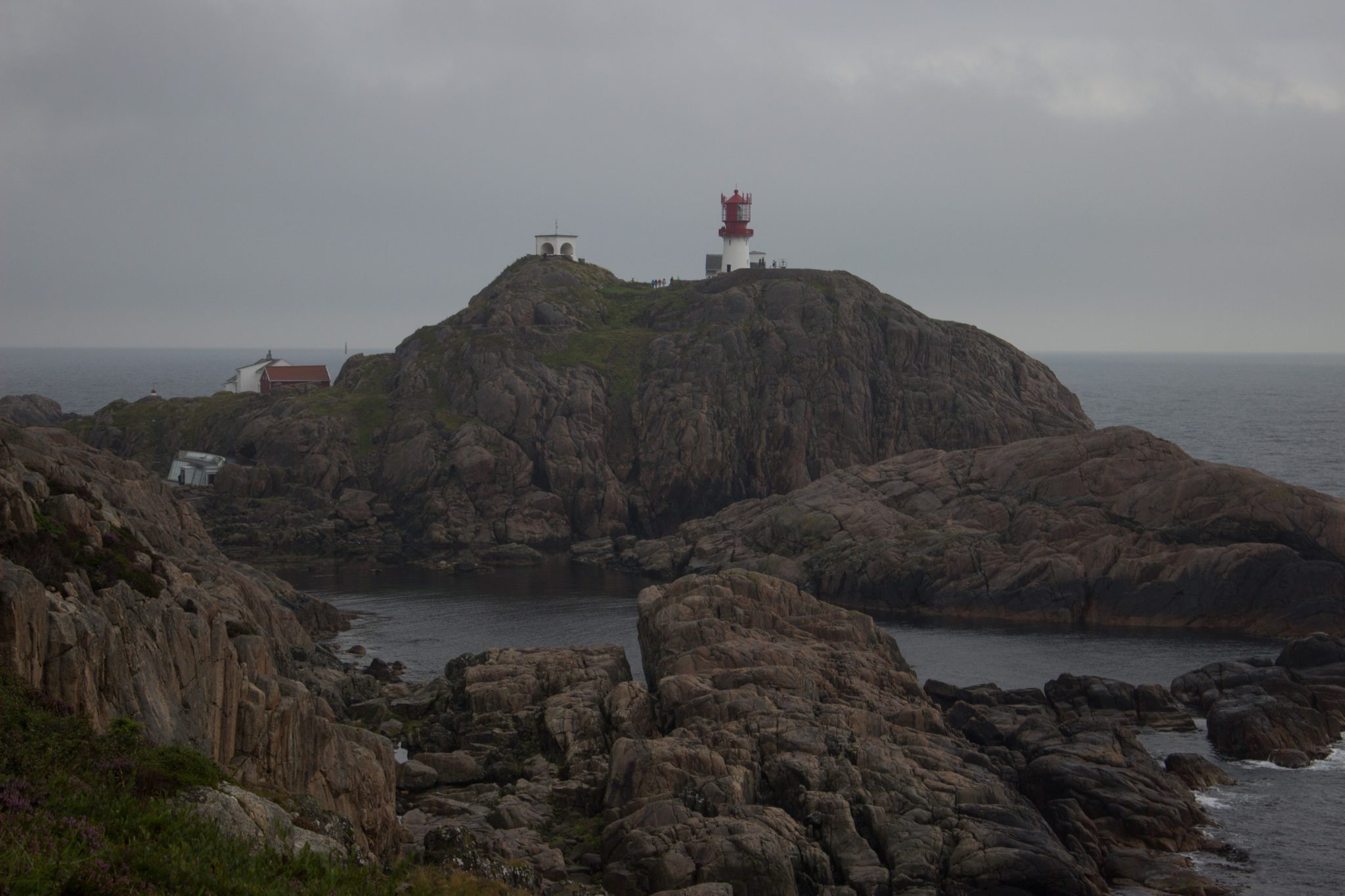 Wanderungen beim Kap Lindesnes, südlichster Punkt Norwegens, am Südkap in Norwegen, Wanderer im Regen unterwegs auf schmalem Pfad entlang großer Felsen, teils sehr sumpfiger Weg, grüne Vegetation an der Küste, Aussicht auf das weite Meer und den Leuchtturm Lindesnes Fyr