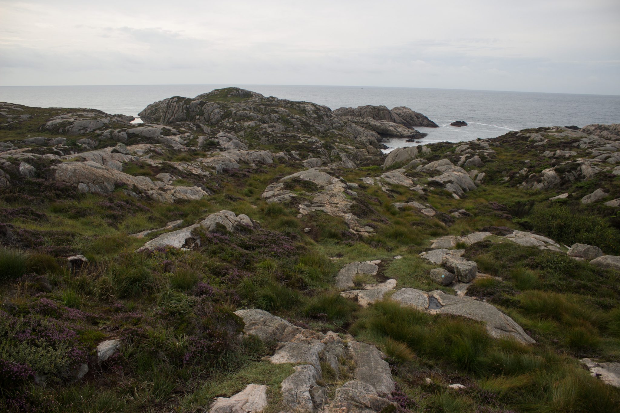Wanderungen beim Kap Lindesnes, südlichster Punkt Norwegens, Leuchtturm Lindesnes Fyr am Südkap in Norwegen, Wanderer unterwegs auf schmalem Pfad entlang großer Felsen, grüne Vegetation an der Küste, Heidelandschaft, Aussicht auf das weite Meer