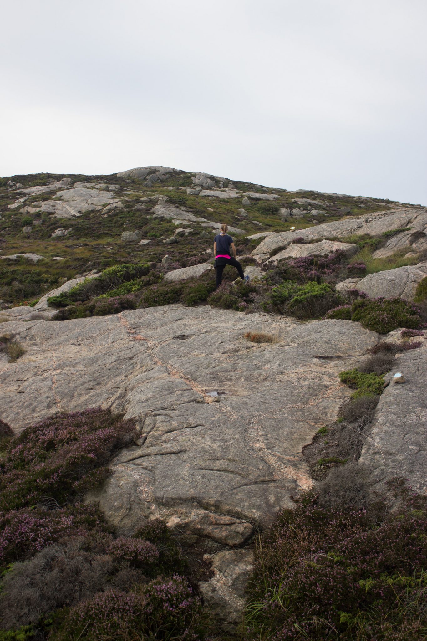 Wanderungen beim Kap Lindesnes, südlichster Punkt Norwegens, Leuchtturm Lindesnes Fyr am Südkap in Norwegen, Wanderer unterwegs auf schmalem Pfad entlang und über große Felsen, grüne Vegetation an der Küste, Heidelandschaft