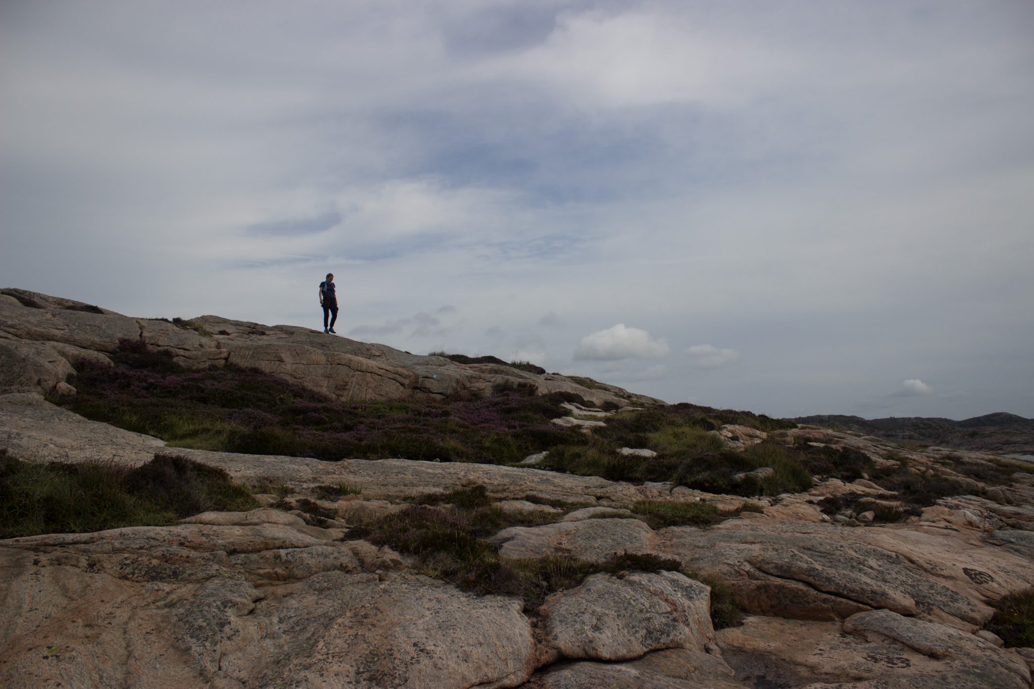 Wanderungen beim Kap Lindesnes, südlichster Punkt Norwegens, Leuchtturm Lindesnes Fyr am Südkap in Norwegen, Wanderer unterwegs auf schmalem Pfad entlang und über große Felsen, grüne Vegetation an der Küste, Heidelandschaft