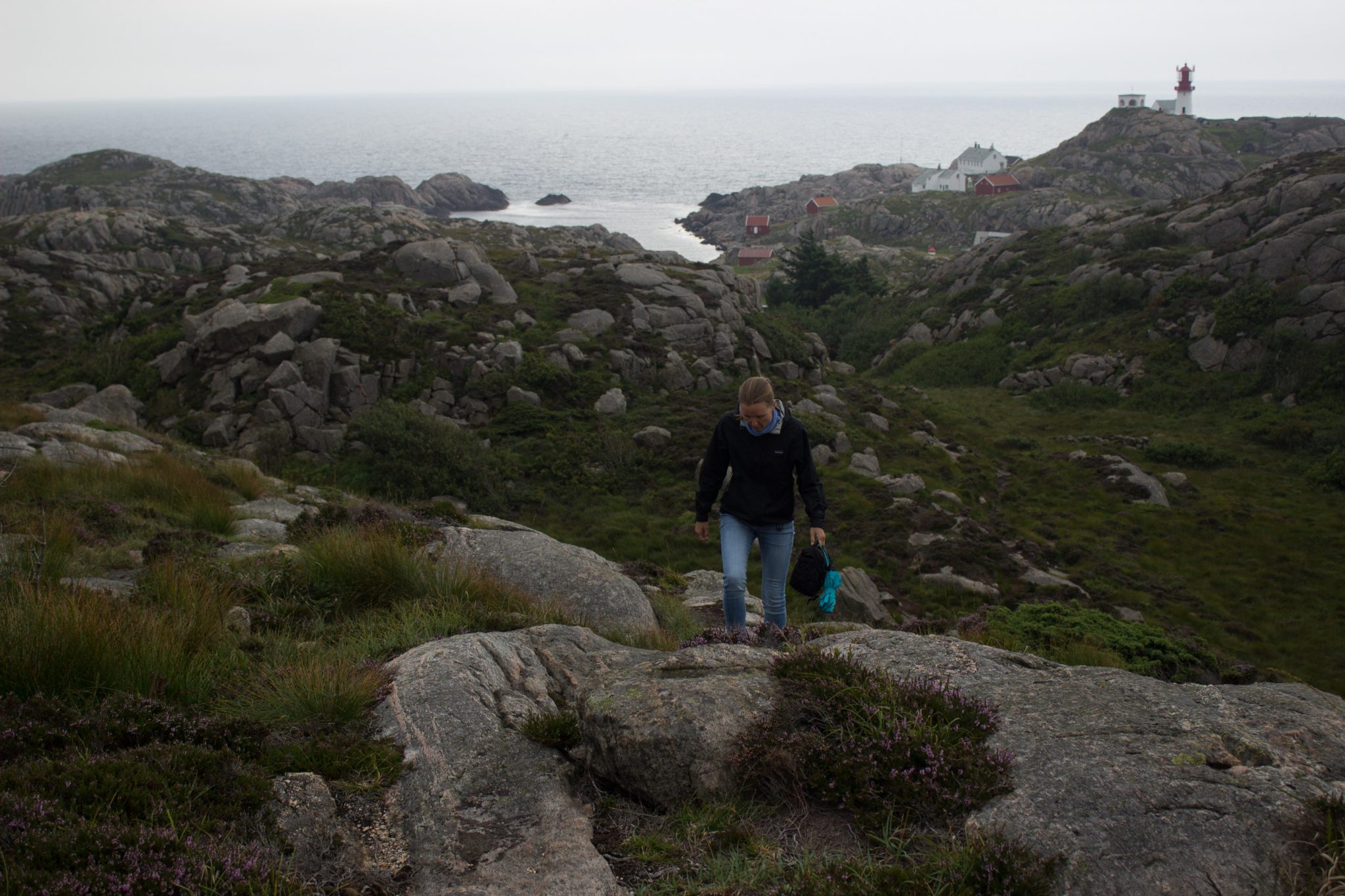 Wanderungen beim Kap Lindesnes, südlichster Punkt Norwegens, am Südkap in Norwegen, Wanderer unterwegs auf schmalem Pfad entlang großer Felsen, grüne Vegetation an der Küste, Heidelandschaft, im Hintergrund der Leuchtturm Lindesnes Fyr und das Meer