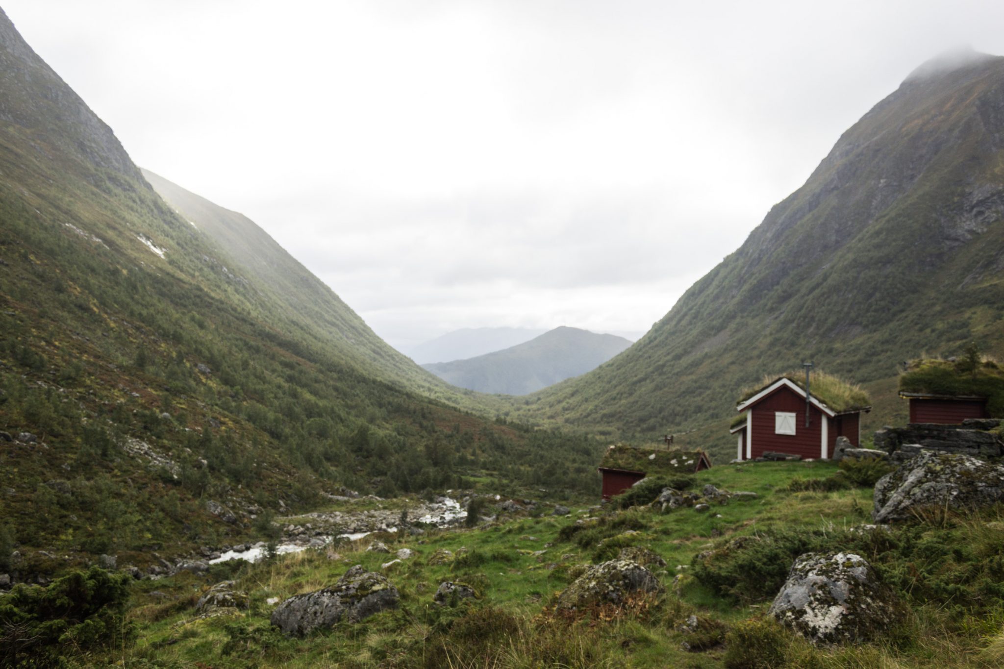 Wanderung im Naturreservat Skorgeura, Naturschutzgebiet in Norwegen, Wanderweg führt entlang eines Baches durch schönes Tal, beiderseits aufragende Berge, kleine Hütten mit bewachsenen Dächern